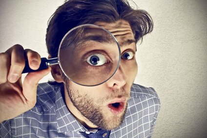 Mann hält eine Lupe vor sein Auge, das vergrößert erscheint. Symbolbild für Sehprobleme und Kurzsichtigkeit. Mann hält eine Lupe vor sein Auge, das vergrößert erscheint. Symbolbild für Sehprobleme und Kurzsichtigkeit.